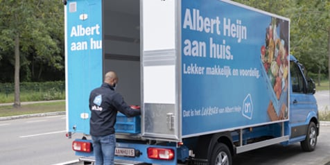 Albert Heijn bezorgwagen voor thuisbezorging met werknemer die de vrachtwagen inlaadt, promotie met tekst "Albert Heijn aan huis. Lekker makkelijk en voordelig."