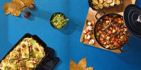 Borden met herfstmaaltijden op een blauwe tafel, inclusief een ovenschotel en een stoofpot met groenten.