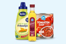 Fles Remia fritessaus, fles AH olijfolie en pak AH tomatensoep naast elkaar geplaatst.