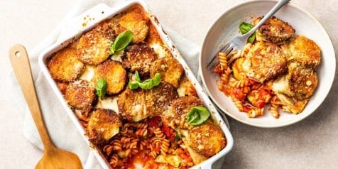 Ovenschotel met aubergine en fusilli pasta in tomatensaus, gegarneerd met verse basilicum.