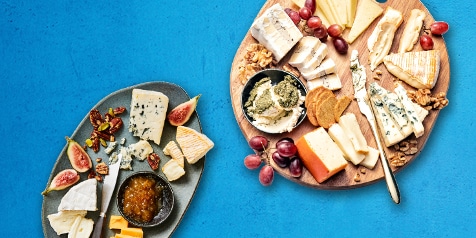 Kaasplank met diverse kazen, druiven, vijgen en noten op een blauwe achtergrond.