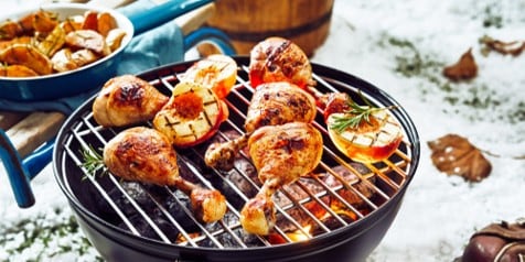 Grill met gegrilde kippenbouten en appels op een sneeuwachtig winterlandschap.