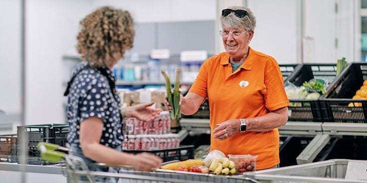 Albert Heijn medewerker helpt klant bij het inpakken van boodschappen met verse groenten en fruit.