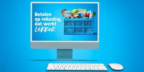 Afbeelding van een computer met een Albert Heijn blauwe krat gevuld met diverse boodschappen, zoals brood, groente, fruit en melk, op het scherm. Op het scherm staat de tekst: "Betalen op rekening, dat werkt lekker". Op de voorgrond staan een toetsenbord en een muis, allemaal op een blauwe achtergrond.