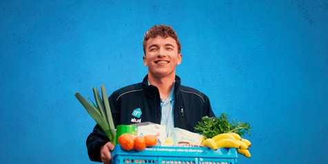 Albert Heijn medewerker met boodschappenkrat gevuld met verse groente en fruit.
