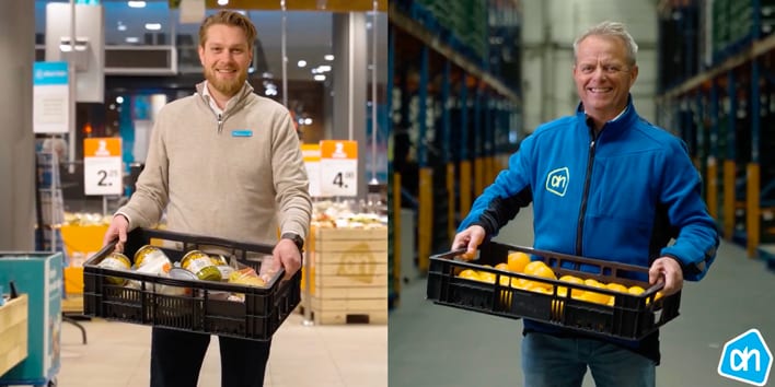 Twee Albert Heijn medewerkers dragen kratten met groenten en fruit in een winkel en magazijnomgeving