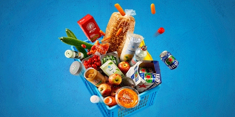 Blauwe boodschappenmand gevuld met diverse producten zoals brood, appels, melk, sap, chips, en knakworsten.