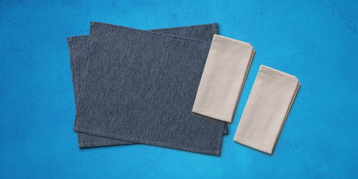 Tafelkleedset bestaande uit donkergrijze placemats en beige servetten op een blauwe achtergrond.