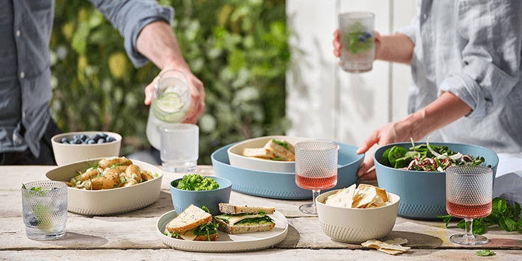 Buitenpicknick met sandwiches, salades, chips en drankjes op een houten tafel.