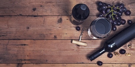 Fles rode wijn met een glas, een wijnopener en een tros druiven op een houten tafel.