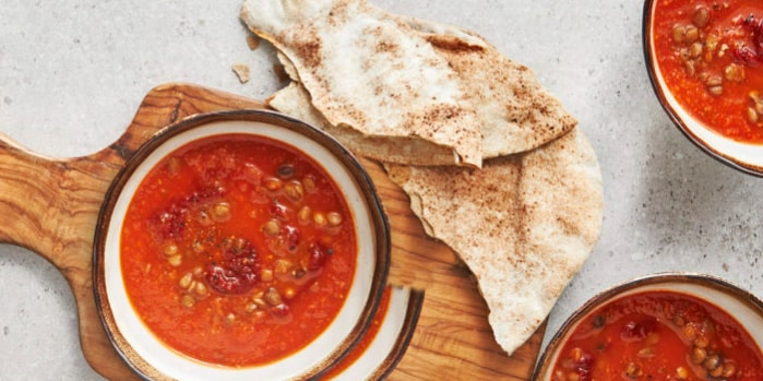Tomatensoep met linzen geserveerd met flatbread op een houten plank.