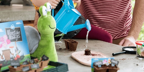 Kind speelt met Moestuintjes-set van Albert Heijn en giet water op aarde in kleine potten, naast groene speelgoedslak.