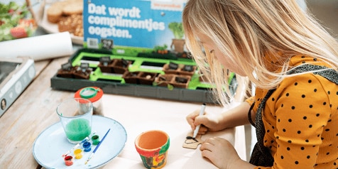 Kind schildert met verf aan tafel bij Albert Heijn tuinproject.