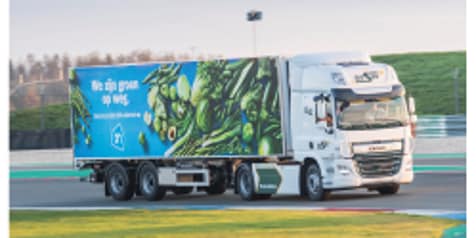 Albert Heijn vrachtwagen met groene slogan "We zijn groen op weg" en afbeeldingen van groenten op de zijkant van de trailer.