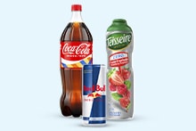 Fles Coca-Cola, blikje Red Bull en fles Teisseire aardbeiensiroop naast elkaar op een lichte achtergrond