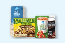 AH rijstwafels naturel, Nature Valley proteinreep, AH tomatensoep beker en een flesje chocolade proteïnedrank op een lichte achtergrond.