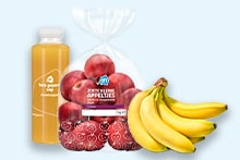 Zak met rode appels, tros bananen en een fles verse jus d'orange van Albert Heijn op een lichte achtergrond.
