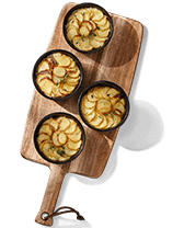 Vier schaaltjes met aardappelgratin op een houten serveerplank.