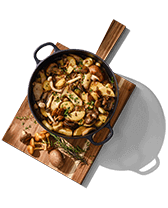 Gietijzeren pan met gebakken aardappelen en paddenstoelen op een houten plank