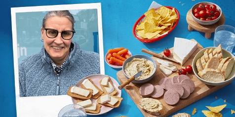 Borrelplank met hapjes waaronder kaas, worst, hummus, cherrytomaatjes, wortels, chips en glazen water.