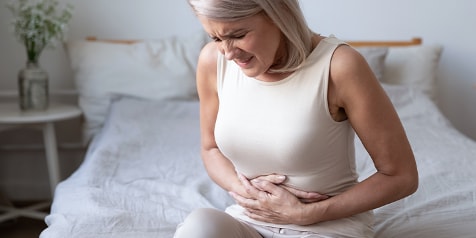 Vrouw met buikpijn zittend op bed