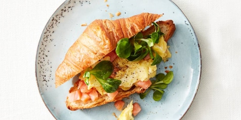 Croissant met zalm, ei en sla op een lichtblauwe schotel.