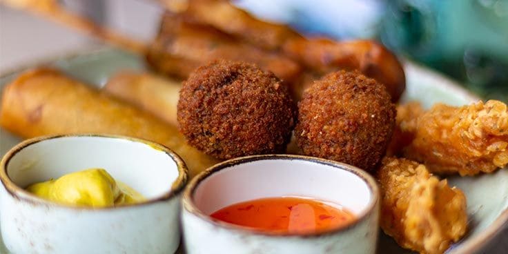 Assortiment van gefrituurde hapjes met mosterd- en chilisaus.