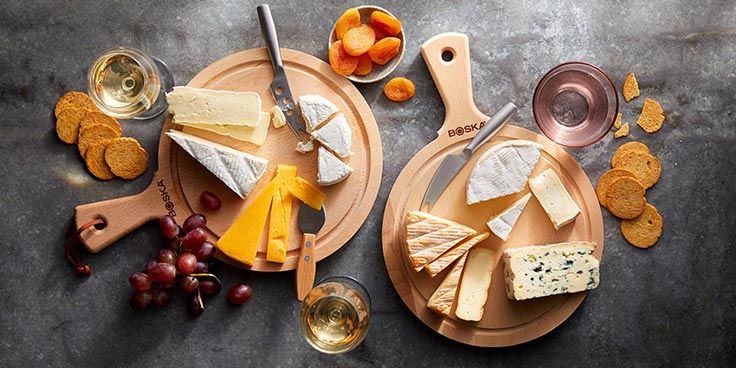 Kaasplankjes met diverse kazen, druiven, abrikozen, crackers en glazen witte wijn.