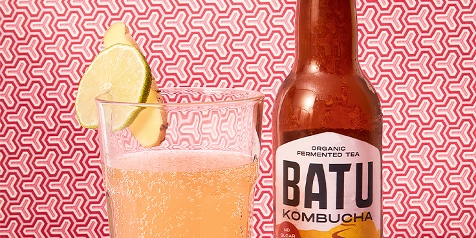Batu Kombucha fles en glas met schijfje limoen op een rood patroon.