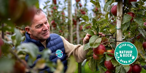 Man in een appelboomgaard met rode appels, zichtbaar met het "Beter voor Natuur & Boer"-keurmerk.
