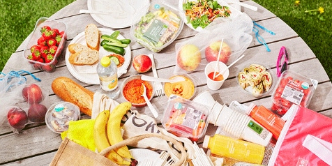 Picknicktafel met verschillende voedselproducten, waaronder salades, brood, fruit en drankjes van Albert Heijn.