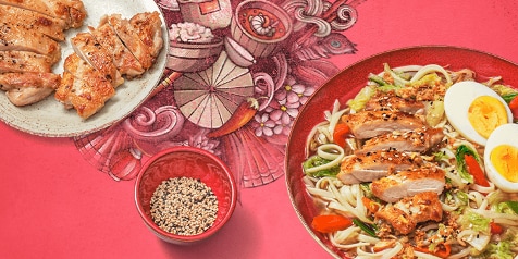 Bord met gesneden kip, noedels, groenten en een hardgekookt ei, naast een schotel gebakken kip en een kom met sesamzaadjes op een kleurrijke achtergrond.