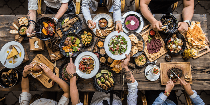 Bovenaanzicht van een rijkelijk gedekte tafel met diverse gerechten en mensen die samen eten delen.