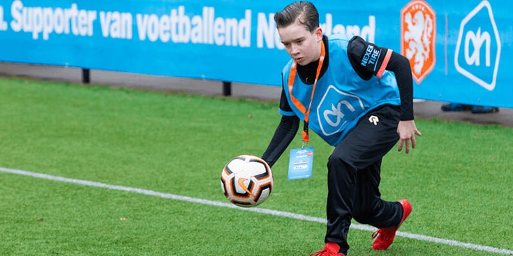 Kind traint met voetbal op veld met Albert Heijn logo zichtbaar