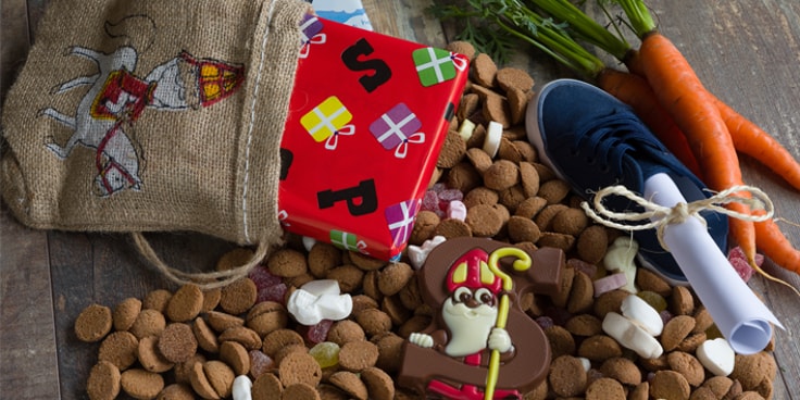 Sinterklaasfeest tafel met pepernoten, wortels, een geschenkdoos, een jute zak en een Sinterklaas chocoladefiguur.