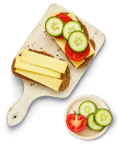 Volkorenbrood met kaas, komkommer en tomaat op een snijplank, met een schaaltje komkommerschijfjes en een halve tomaat.
