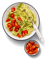 Spaghetti met pesto en cherrytomaten in een witte kom, geserveerd met extra cherrytomaten in een klein schaaltje ernaast.