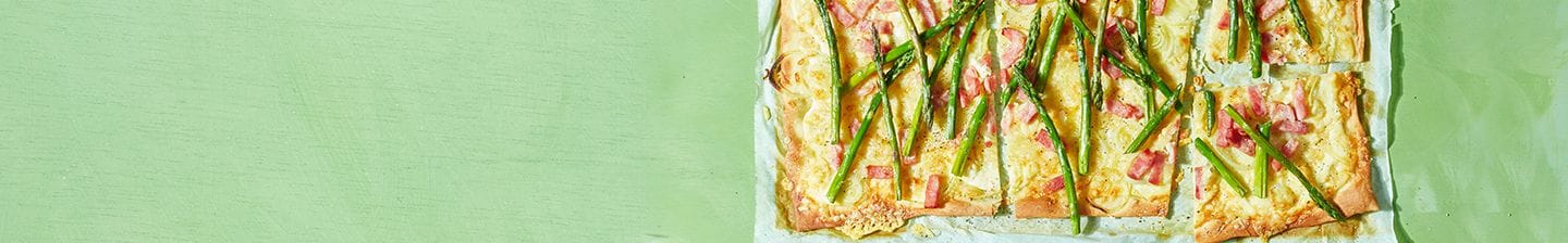 Flammkuchen met asperges en spekjes op een groen oppervlak