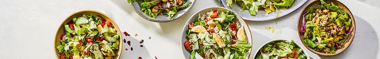 Verschillende schalen met kleurrijke salades op een witte achtergrond.