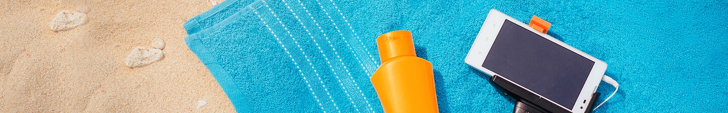 Strand scene met blauwe handdoek, zonnebrandcrème en smartphone