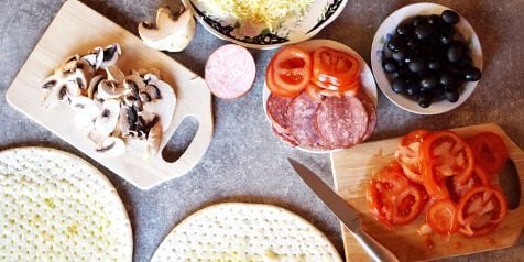 Ingrediënten voor het maken van pizza, inclusief champignons, salami, tomaten, zwarte olijven en geraspte kaas.