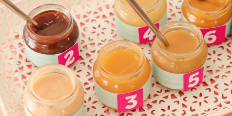 Verschillende potjes babyvoeding met lepeltjes en genummerde etiketten op een dienblad.