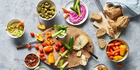 Borrelplank met diverse groenten, olijven, hummus, dips, brood en kaas.