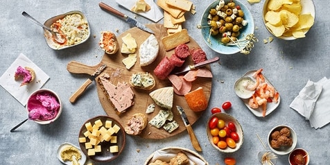 Assortiment van hapjes en snacks op een houten plank, inclusief kaasblokjes, vleeswaren, olijven en een selectie spreads.