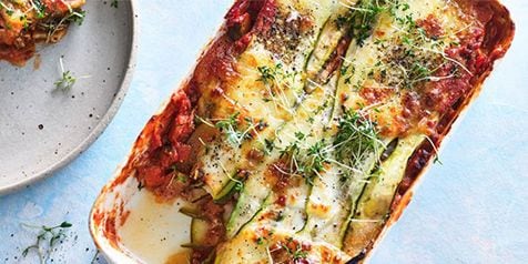 Vegetarische lasagne met courgette en kaas, gegarneerd met verse kruiden in een ovenschaal.