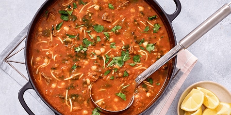 Harira soep in een pan met verse peterselie bovenop en een lepel erin.