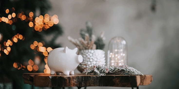 Wit spaarvarken op houten tafel met kerstdecoratie en warme sfeerverlichting op de achtergrond