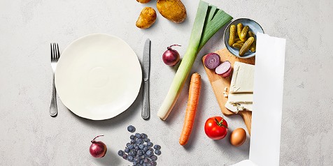 Ongesneden groenten en fruit, met een bord en bestek, op een tafel geplaatst.