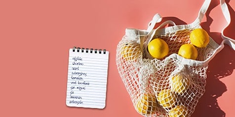 Netzak met citroenen naast boodschappenlijstje op een roze achtergrond.