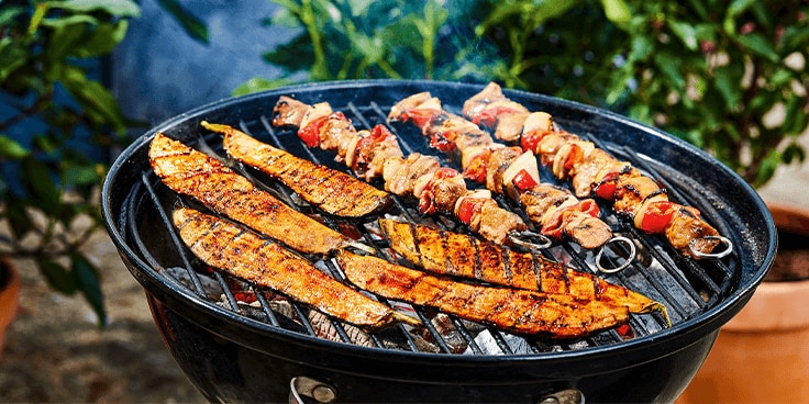 Vis en vlees spiesjes op de barbecue met een achtergrond van groen bladerdek.